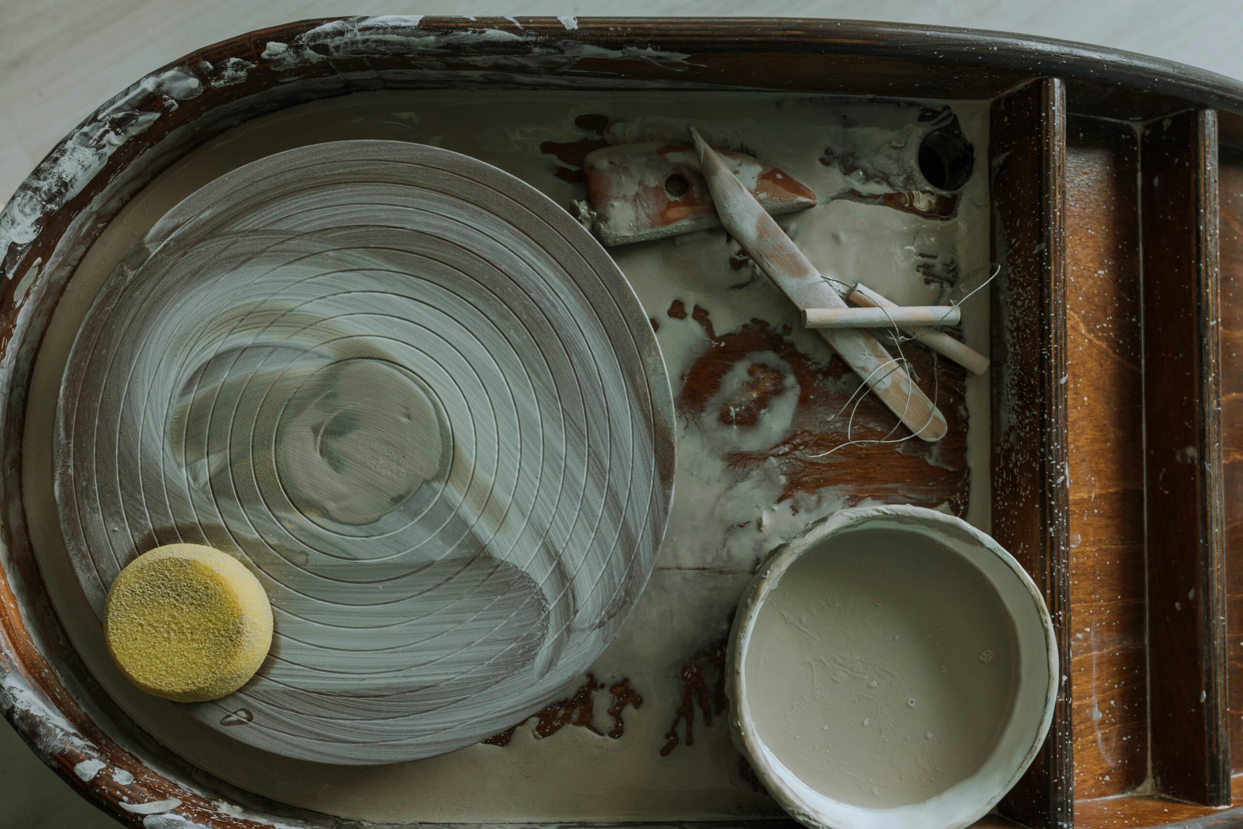 Image d'un tour de potier avec des outils. Eponge, estèque en bois, fil à beurre, barbotine